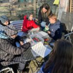 Das Foto zeigt die Auszubildende Kristina mit Kindern an einem Tisch, die Kinder füllen Blätter aus.