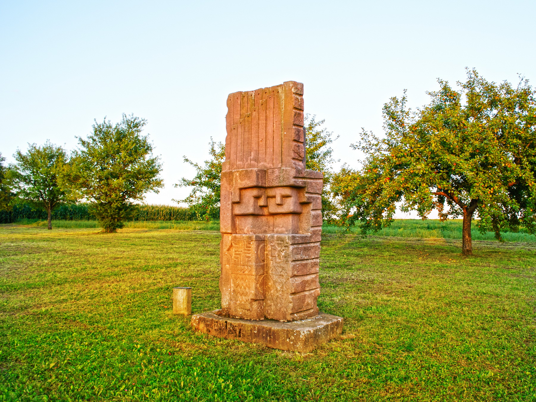 This photo shows a rectangular stone sculpture with different carvings in front of trees.