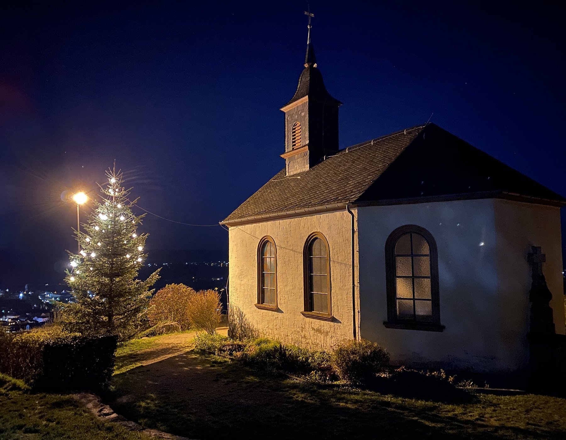 Das Foto zeigt die Kreuzbergkapelle bei Nacht, der Tannenbaum vor der Kapelle ist beleuchtet.