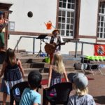 Das Foto zeigt Clown Lolek und Kinderliedermacher Casi bei ihrem Auftritt im Rahmen des Merziger Kindersommers 2021 vor dem Kinderpublikum im Innenhof des Rathauses.