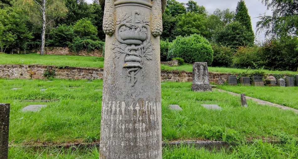 Das Bild zeigt die Gedenksäule für Alfred Kaufmann auf dem jüdischen Friedhof. Diese zeigt einen Äskulapstab und eine Inschrift.