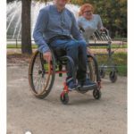Das Foto zeigt den Titel des neuen Flyers "barrierearmes Merzig", darauf zu sehen ist ein junger Mann im Rollstuhl sowie eine Frau mit einem Rollator vor dem Brunnen im Stadtpark.
