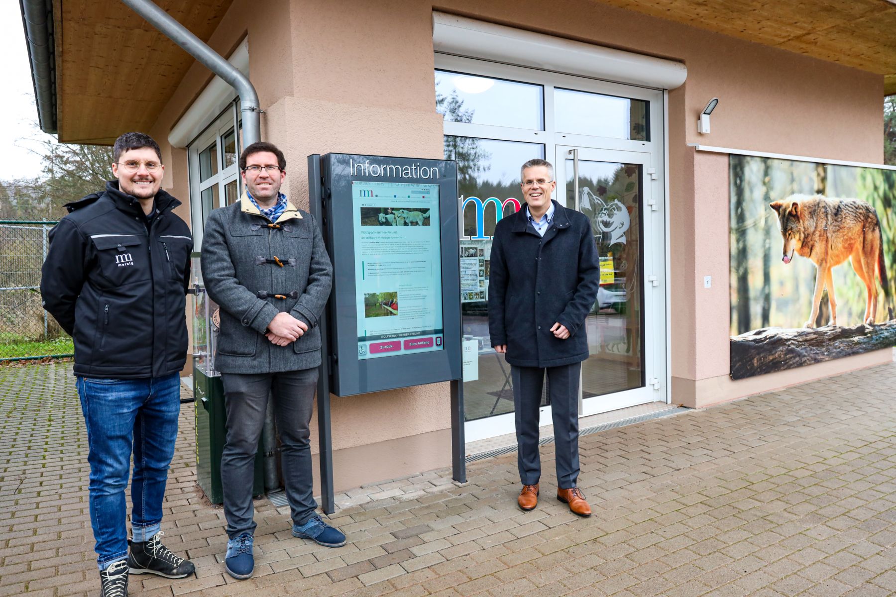 Das Foto zeigt das Info-Terminal. Links davon steht der Bürgermeister der Kreisstadt Merzig, Marcus Hoffeld. Rechts davon stehen zwei weitere Personen.