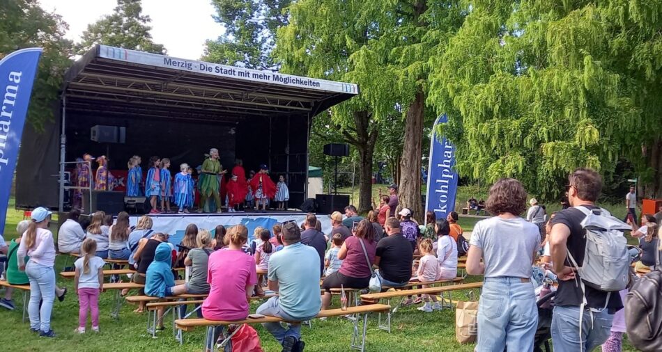 Das Foto zeigt zahlreiche Kinder, die vor der Bühne sitzen, und dem Mitmachtheater anschauen.