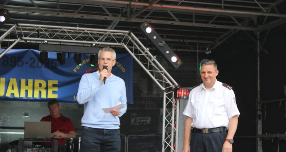 Oberbürgermeister Marcus Hoffeld und Löschbezirksführer Jürgen Lamest auf der Bühne, Marcus Hoffeld hat ein Mikrofon in der Hand