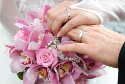 Auf einem Blumenstrauß liegen zwei Hände, die Frau umklammert die Hand des Mannes