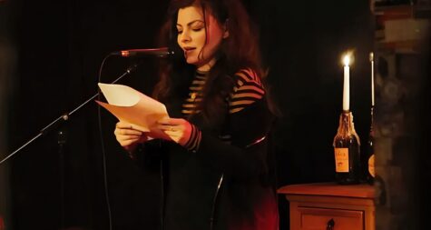 Jenny Theobald hält Blätter in der Hand und spricht in ein Mikrofon, alles wirkt sehr düster