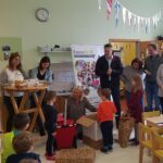 Kinder und Erwachsene in einem Kindergartenraum, Kinder packen Geschenke aus