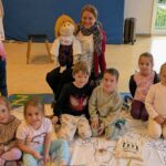 Kinder sitzen auf einer Decke, Frau mit Handpuppe sitzt dabei, Kinder halten Plakate