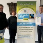 Christian Bies, Pia Schäfer und Marcus Hoffeld mit Urkunde, Banner und Merchandise