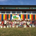 Schülerinnen und Schüler mit Schulbuchtaschen vor einem bunten Gebäude