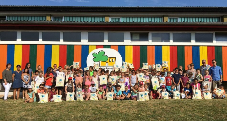 Schülerinnen und Schüler mit Schulbuchtaschen vor einem bunten Gebäude