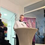 Oberbürgermeister Marcus Hoffeld spricht ins Mikrofon, eine Fernsehkamera ist auf ihn gerichtet, neben ihm steht Minister Jost