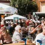 zwei Foodtrucks und ein Pavillon, im Vordergrund sitzen und stehen viele Menschen