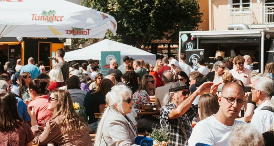 zwei Foodtrucks und ein Pavillon, im Vordergrund sitzen und stehen viele Menschen