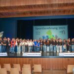 Zahlreiche Sportlerinnen und Sportler, die bei der Sportlerehrung 2025 geehrt wurden. Sie stehen auf der Bühne und halten ein Geschenk in der Hand.