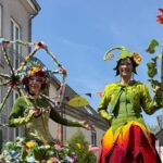 Stelzenläuferinnen mit großer Blume und Schirm aus Blumen