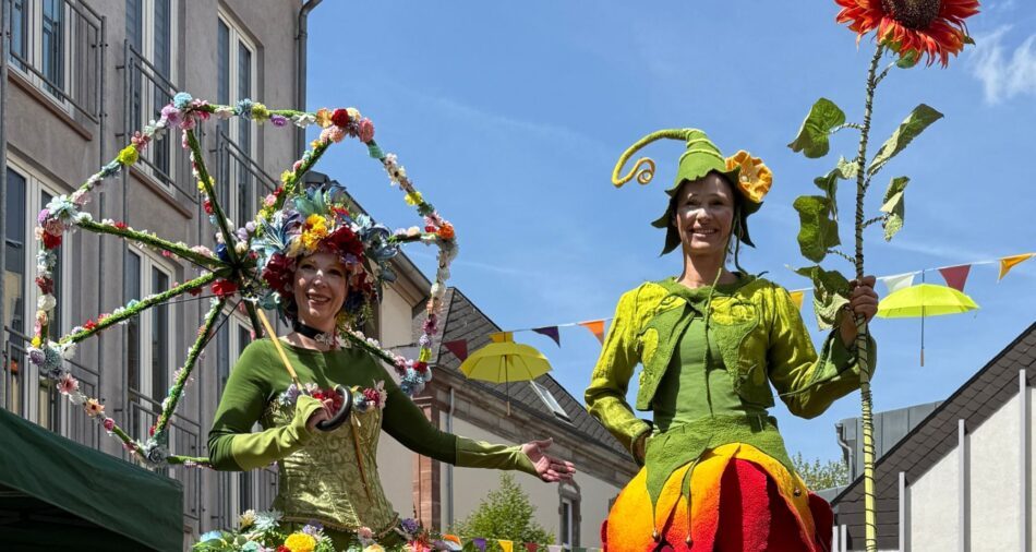 Stelzenläuferinnen mit großer Blume und Schirm aus Blumen