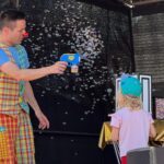Mann in buntem Clownskostüm sprüht Seifenblasen auf der Bühne