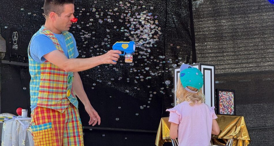 Mann in buntem Clownskostüm sprüht Seifenblasen auf der Bühne