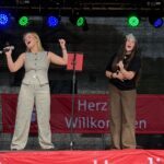 Zwei junge Frauen stehen auf einer Bühne und singen, beide alten ein Mikrofon in der Hand