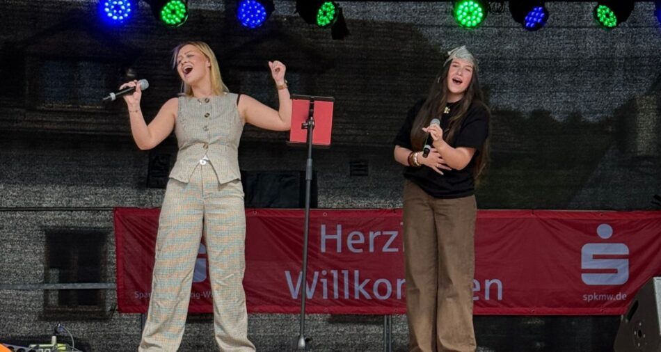 Zwei junge Frauen stehen auf einer Bühne und singen, beide alten ein Mikrofon in der Hand