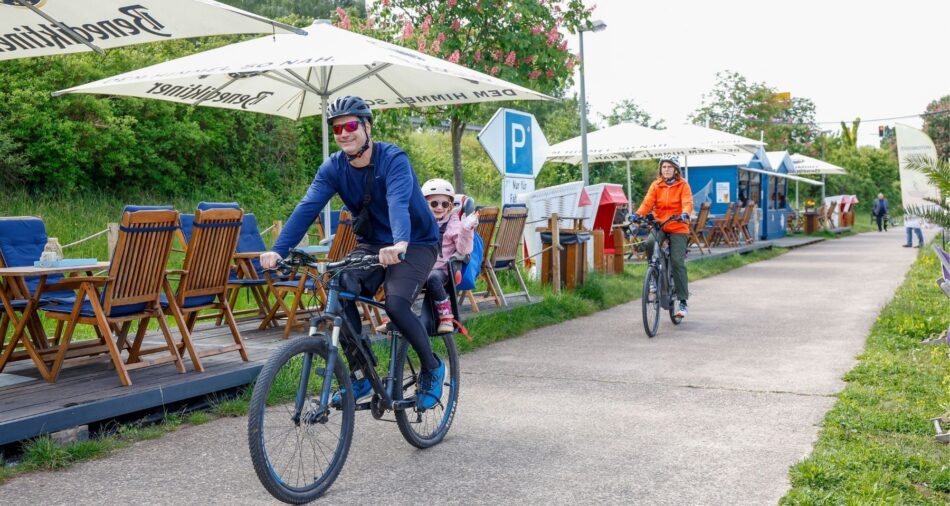 Mann auf Fahrrad, kleines Mädchen im Kindersitz, winkt fröhlich in die Kamera