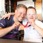 Mann und Junge umarmen sich, Mann zeigt Bronzemedaille des stolzen Jungen in die Kamera