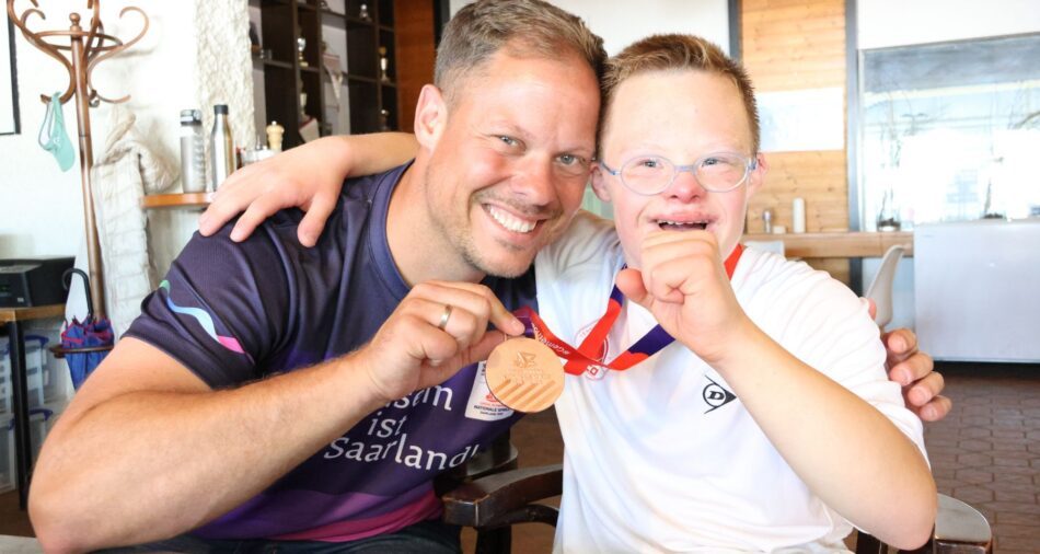 Mann und Junge umarmen sich, Mann zeigt Bronzemedaille des stolzen Jungen in die Kamera