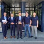 Gruppenfoto mit fünf Herren, sie schauen freundlich in die Kamera, zwei halten Unterlagen in den Händen